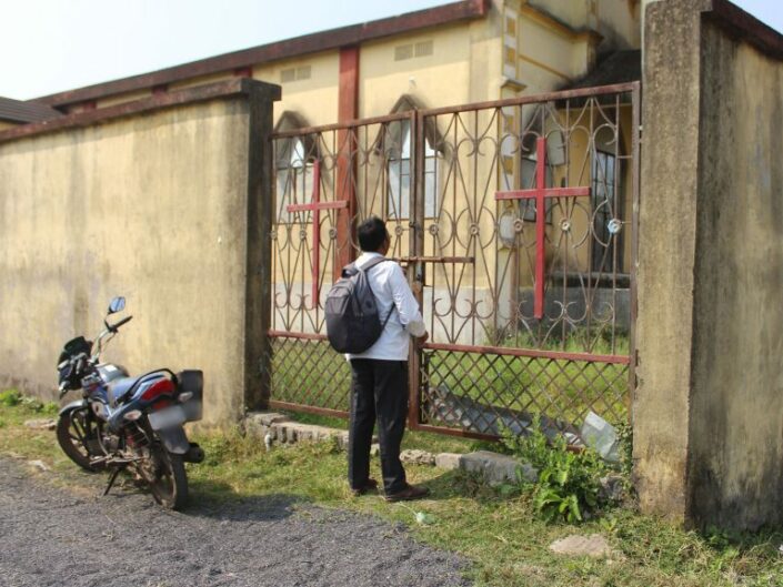 Mies seisoo kirkon suljetulla portilla vieressään moottoripyörä.