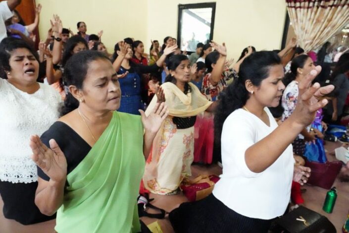 Huone täynnä naisia, jotka ovat kohottaneet kätensä rukoukseen.