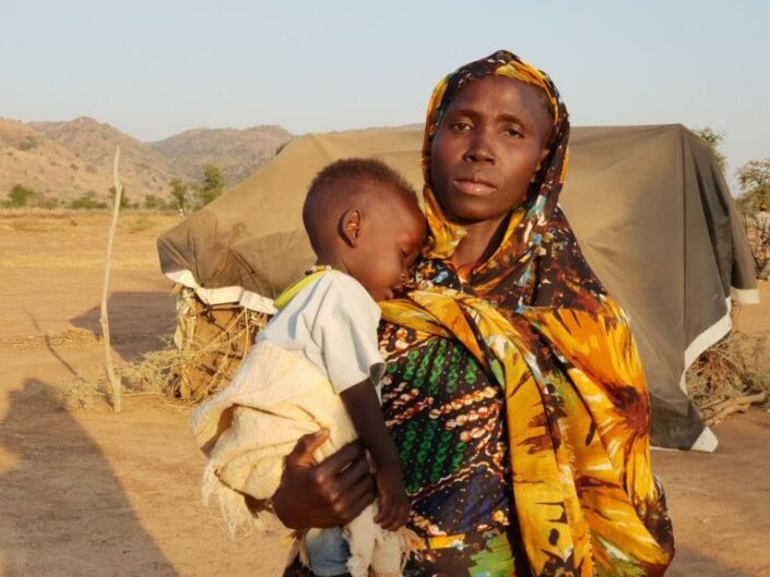 Valokuva sudanilaisesta naisesta nukkuva lapsi sylissään.